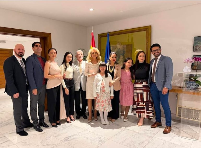 Grupo de diez personas sonrientes en ambiente formal, con elegantes vestimentas, posando en semicírculo y banderas de fondo.