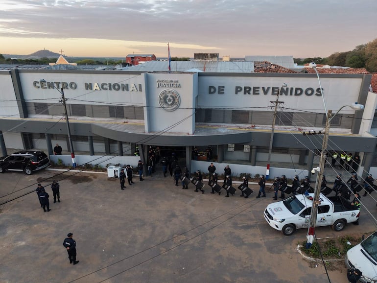 Uniformados de la policía en formación frente al Centro Nacional de Prevención, con vehículos policiales al fondo.