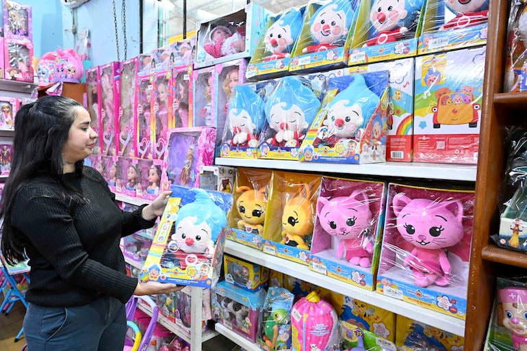 Mujer de cabello largo y lacio sostiene un peluche colorido en tienda repleta de juguetes.