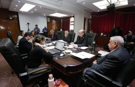 Isaías Ricardo Fretes y José Emilio Argaña Contreras en reunión, con expresión tranquila y ambiente profesional, rodeados de documentos y laptops.