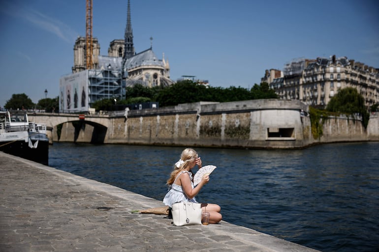 Una persona se abanica mientras está sentada a orillas del río Sena, detrás de la catedral de Notre-Dame en París, durante una ola de calor temprana y récord que azota amplias zonas de Europa occidental el 28 de mayo de 2026.