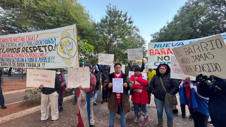 Grupo de manifestantes con chaquetas y vaqueros, algunos levantan carteles en una protesta pacífica en un parque urbano.