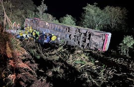 Rescatistas en uniformes amarillos trabajando alrededor de un autobús volcado en un área boscosa, luces de rescate iluminando la escena.