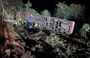 Rescatistas en uniformes amarillos trabajando alrededor de un autobús volcado en un área boscosa, luces de rescate iluminando la escena.
