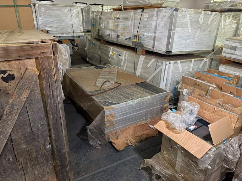 Almacén desordenado con cajas y pallets de equipos médicos deteriorados, sin personas visibles.