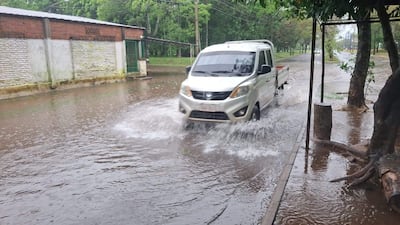 Un vehículo utilitario blanco atraviesa una calle inundada entre paredes de ladrillo y cemento en un entorno residencial