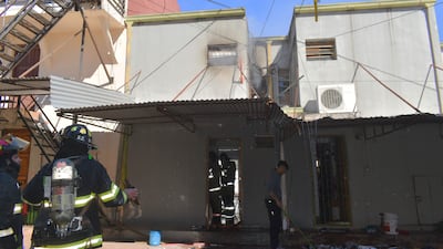 Tres bomberos en trajes de protección con cascos, uno sostiene un hacha mientras un civil en sudadera gris realiza tareas de limpieza.