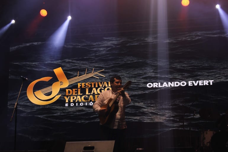 Orlando Evert en el escenario con guitarra, frente a un micrófono y un fondo colorido del festival.