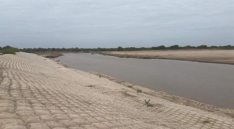 Río Pilcomayo fluye rodeado de sacos de arena, en un paisaje natural con cielo nublado y vegetación escasa.