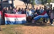 Grupo de personas con banderas de Paraguay en un ambiente rural, escuchando a un hombre con camiseta a rayas que habla en el centro.