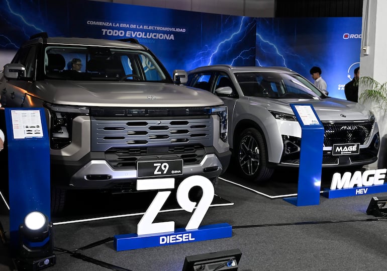 Dos automóviles, Z9 DIESEL y MAGÉ HEV, son presentados en un entorno de exhibición tecnológica, iluminados en un ambiente oscuro.