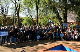 Grupo de unas 100 personas, incluyendo niños, con banderas paraguayas y pancartas en ambiente natural.