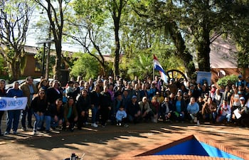 Grupo de unas 100 personas, incluyendo niños, con banderas paraguayas y pancartas en ambiente natural.