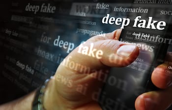 Una mano de hombre sostiene un teléfono celular. Un filtro se superpone con las palabras "deepfake", "hoax", "information", "disinformation".