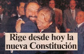 Hombres abrazándose con alegría en un ambiente de celebración, con el texto visible: 'Rige desde hoy la nueva Constitución'.