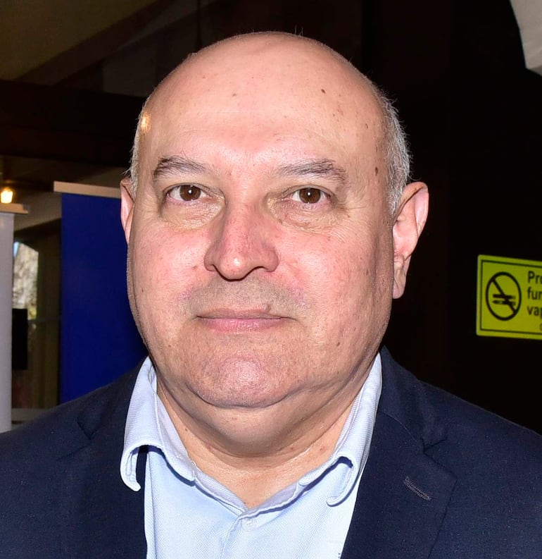 Hombre de mediana edad con cabello canoso y expresión seria, viste camisa clara y chaqueta oscura en un evento formal.