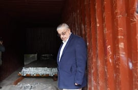 Isaías Fretes con chaqueta oscura y camisa blanca, observa el interior de un contenedor, rodeado de fotógrafos en un ambiente de inspección.
