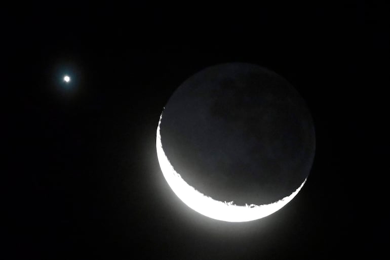 Luna en cuarto creciente en el lado derecho, con un brillante planeta a la izquierda, en un cielo estrellado.
