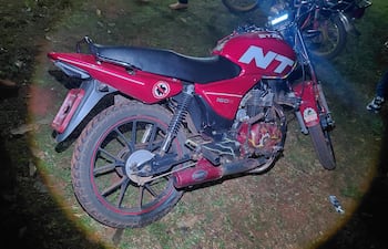 Motocicleta roja modelo NT 150 R iluminada en un entorno nocturno, sin personas visibles en primer plano.