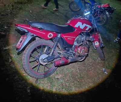 Motocicleta roja modelo NT 150 R iluminada en un entorno nocturno, sin personas visibles en primer plano.