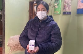Mujer con chaqueta oscura y mascarilla sostiene caja de medicamento. Su expresión es seria y preocupada.
