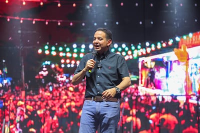 Ricardo Estigarribia Medina en camisa negra y jeans claross sostiene un micrófono ante una multitud iluminada por luces brillantes.