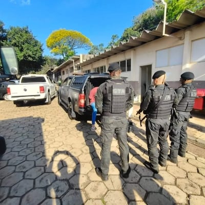 Cuatro agentes de policía con chalecos tácticos rodean a un sospechoso agachado junto a una camioneta negra en un entorno urbano.