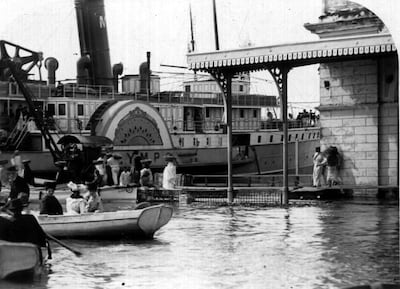 Grupo de personas en muelle, algunas en canoas, abordando barco de vapor conera inscripción 'YM P'. Ropa de época y sombreros.