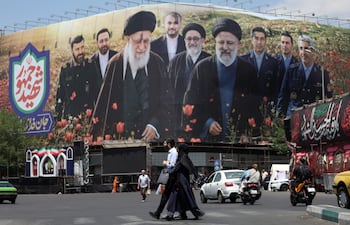 Ciudadanos iraníes caminan frente a una gran valla publicitaria con imágenes del difunto líder supremo iraní, el ayatolá Ali Jamenei, y del difunto presidente iraní, Ebrahim Raisi, en la plaza Enghelab de Teherán, Irán.