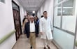 Isaías Fretes, con saco oscuro y camisa blanca, camina junto a Miguel Gómez, en bata blanca, en un pasillo del hospital.