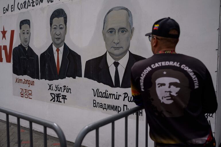 Un miembro de la organización civil "Catedral Combativa", que apoya al régime chavista, observa un mural en el que aparecen los presidentes Kim Jong-Un, de Corea del Norte (i); Vladimir Putin, de Rusia (C) y Xi Jinping, de China (d), en Caracas.