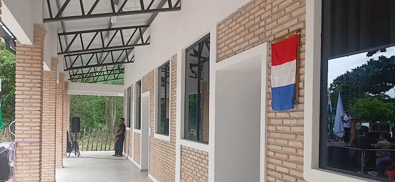 Persona de pie frente a micrófono, habla a un grupo. Ambiente al aire libre con bandera de Paraguay y vegetación.