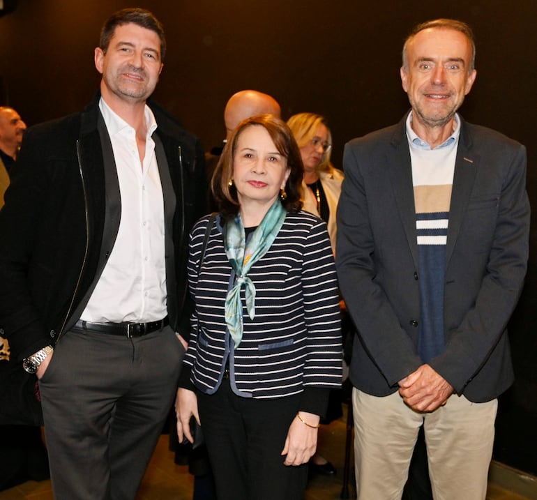 Una mujer de blusa a rayas y pañuelo, junto a dos hombres, uno en chaqueta oscura y otro con saco, conversan en el museo.