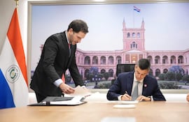 Santiago Peña en traje oscuro firme documentos, Mirtha Alzira Arias Noguer a su lado en traje azul, ambos en oficina gubernamental.