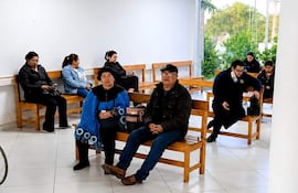 Mujer con vestimenta tradicional azul y negro en el centro, rodeada de pacientes en un ambiente luminoso con plantas.