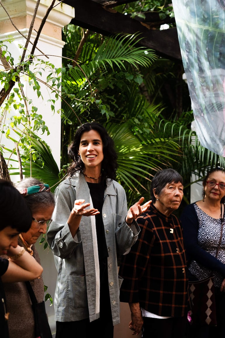 Laura Gorski en chaqueta gris habla mientras otras ceramistas la escuchan atentamente en un entorno natural rodeado de plantas.