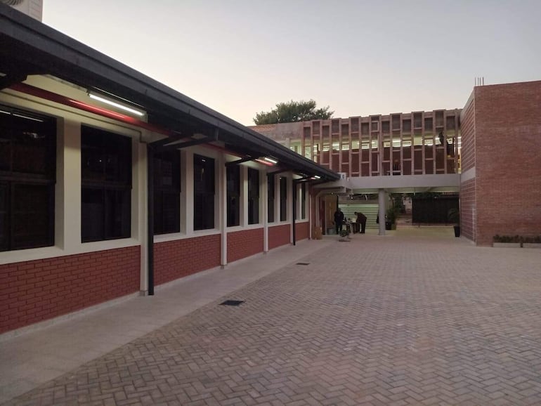 Edificio moderno de dos niveles con paredes de ladrillo y ventanales, pavimento de adoquines en un entorno educativo.