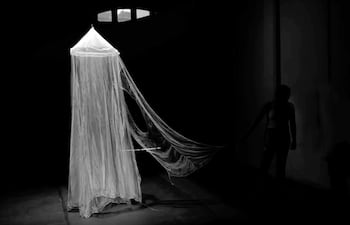 Silueta de una persona de pie junto a un objeto artístico cónico, en un entorno oscuro y misterioso.