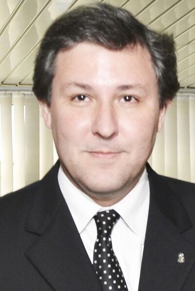 Filizzola en traje formal con corbata, luciendo sereno, participando en un evento con otros asistentes en un ambiente institucional.