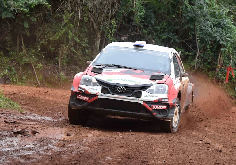Toyota de rally en pista de tierra, cubierto de barro, con logotipos de patrocinadores como Petrobras y Lubrax.