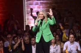Soledad Núñez, con chaqueta verde, sostiene un micrófono mientras la audiencia muestra apoyo levantando los brazos.