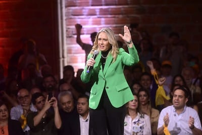 Soledad Núñez, con chaqueta verde, sostiene un micrófono mientras la audiencia muestra apoyo levantando los brazos.