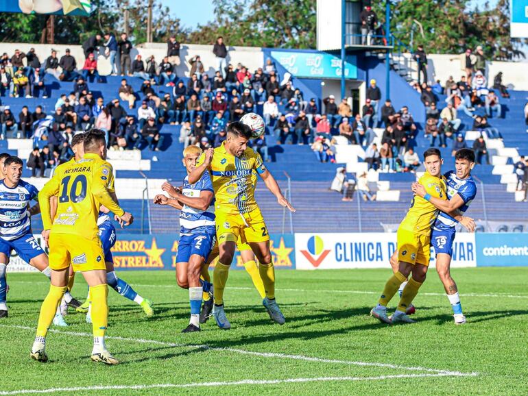 El defensor de Sportivo Trinidense, César Benítez se eleva para despejar de cabeza ente el asecho de Miguel Barreto.