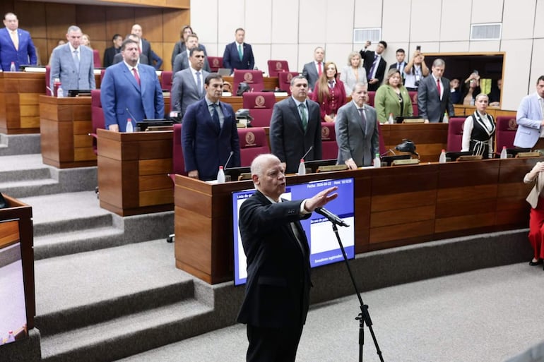 Luis María Benítez Riera en traje negro habla ante senadores atentos, mientras otros miembros observan en el recinto legislativo.