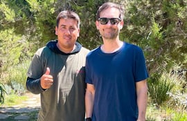 Richard Alfredo Aguilar Delgado en camiseta gris y Tobey Maguire en camiseta azul y gafas, sonriendo y posando en un entorno verde.