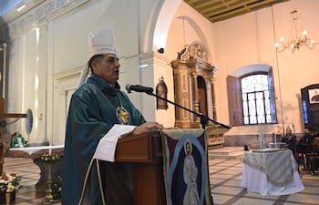 Obispo con manto verde y mitra blanca habla desde un podio con micrófono frente a un altar decorado.
