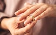 Una mano retira un anillo dorado del dedo anular, en un entorno interior difuminado.