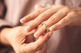 Una mano retira un anillo dorado del dedo anular, en un entorno interior difuminado.
