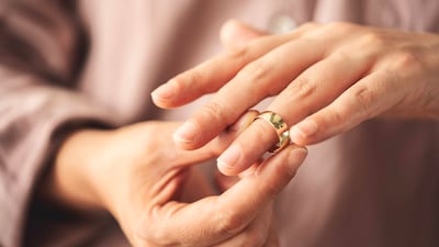 Una mano retira un anillo dorado del dedo anular, en un entorno interior difuminado.