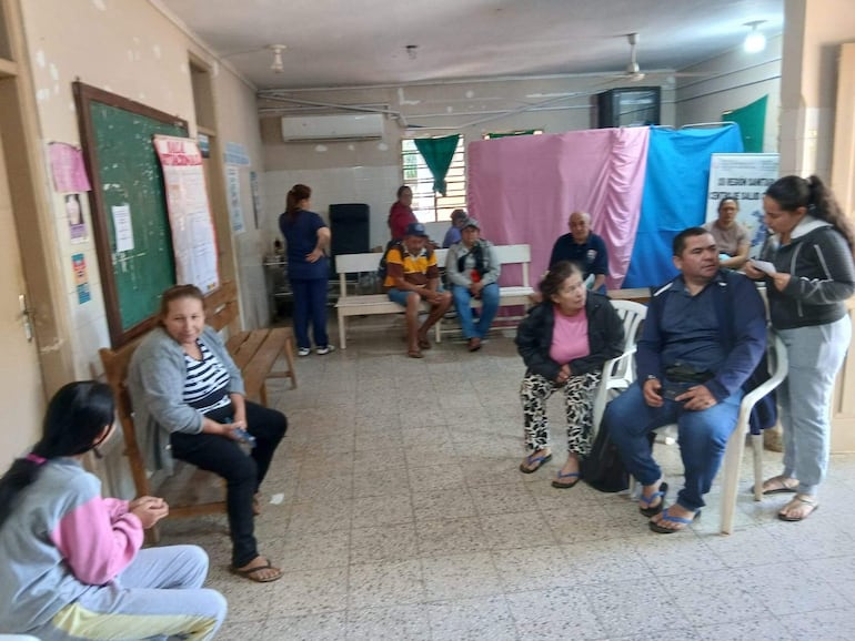 Mujeres y hombres conversan en un ambiente informal, algunos con ropa casual, sentados y de pie en un centro de salud.
